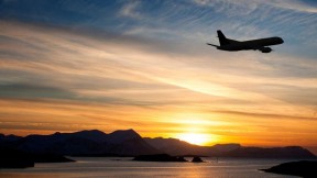 Aircraft taking off over coastal region at sunset